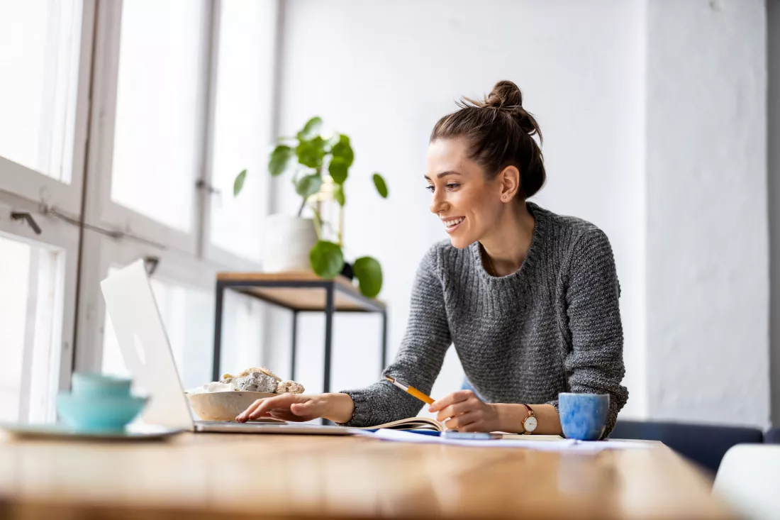 Młoda, uśmiechnięta kobieta pracuje na laptopie w domowym biurze