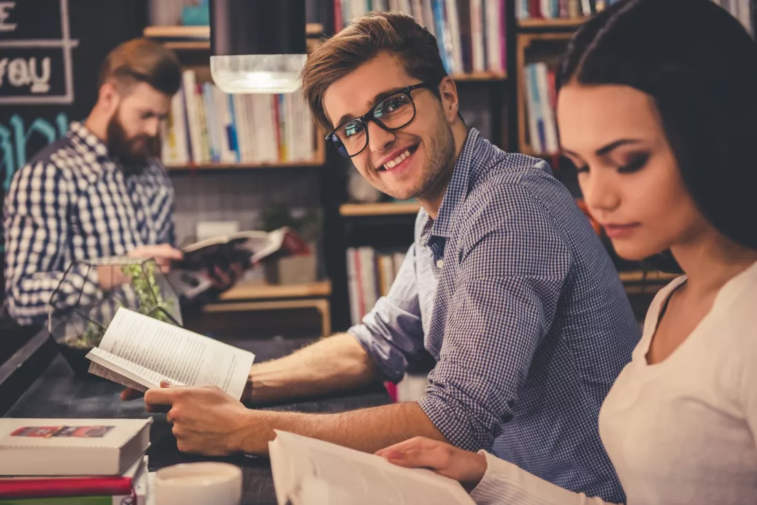 Studenci historii pracują nad książkami przy stole w bibliotece.