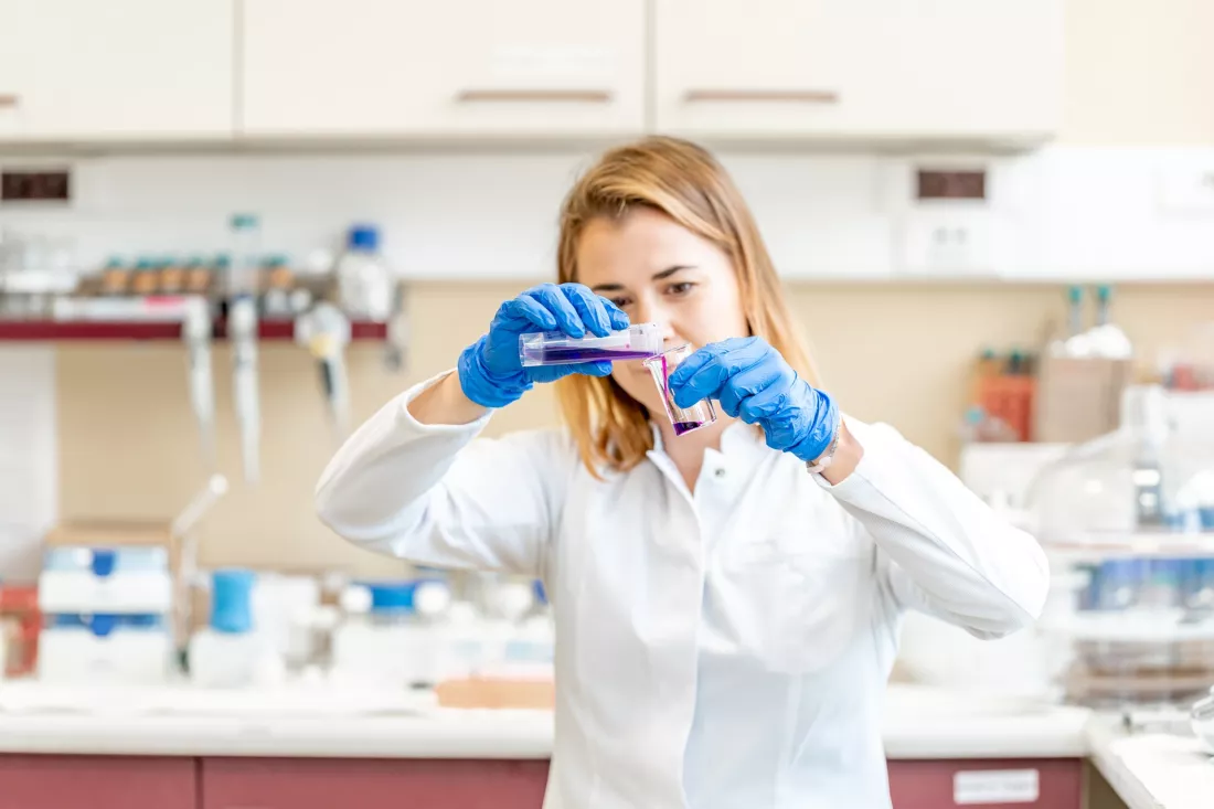 Studentka w fartuchu pracuje przy pipecie w laboratorium chemicznym