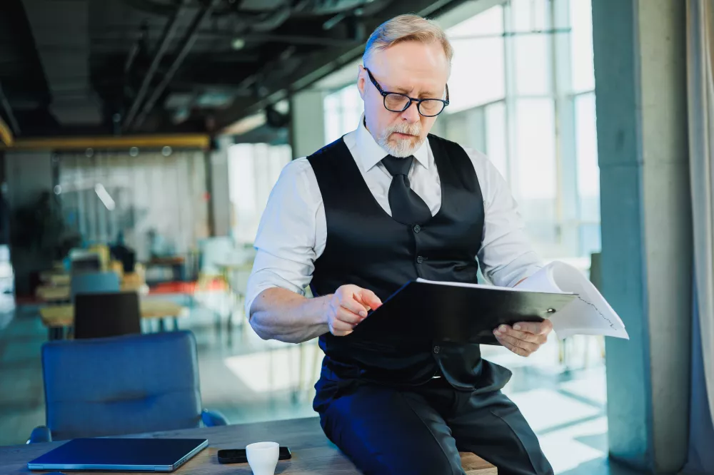 grayhaired-bearded-man-glasses-white-shirt-looks-through-documents-adult-man-is-sitting-desk-office